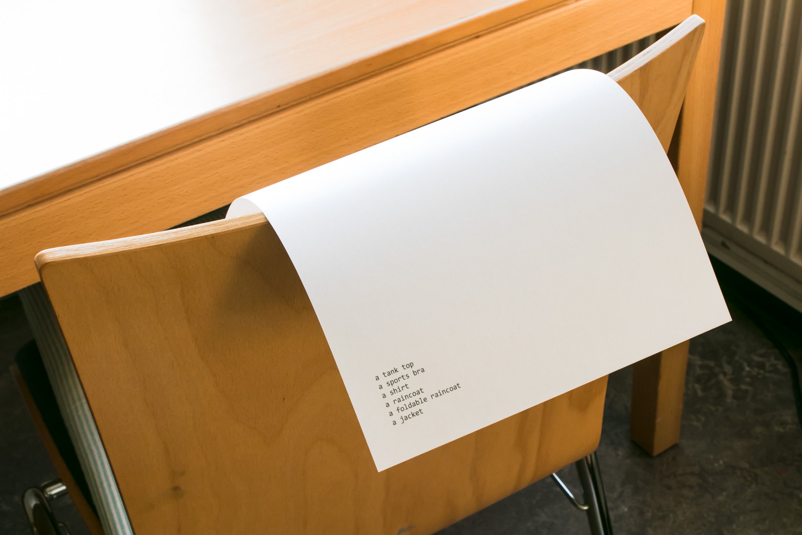 An A4 paper sheet balanced on the back of a chair, listing the objects, 