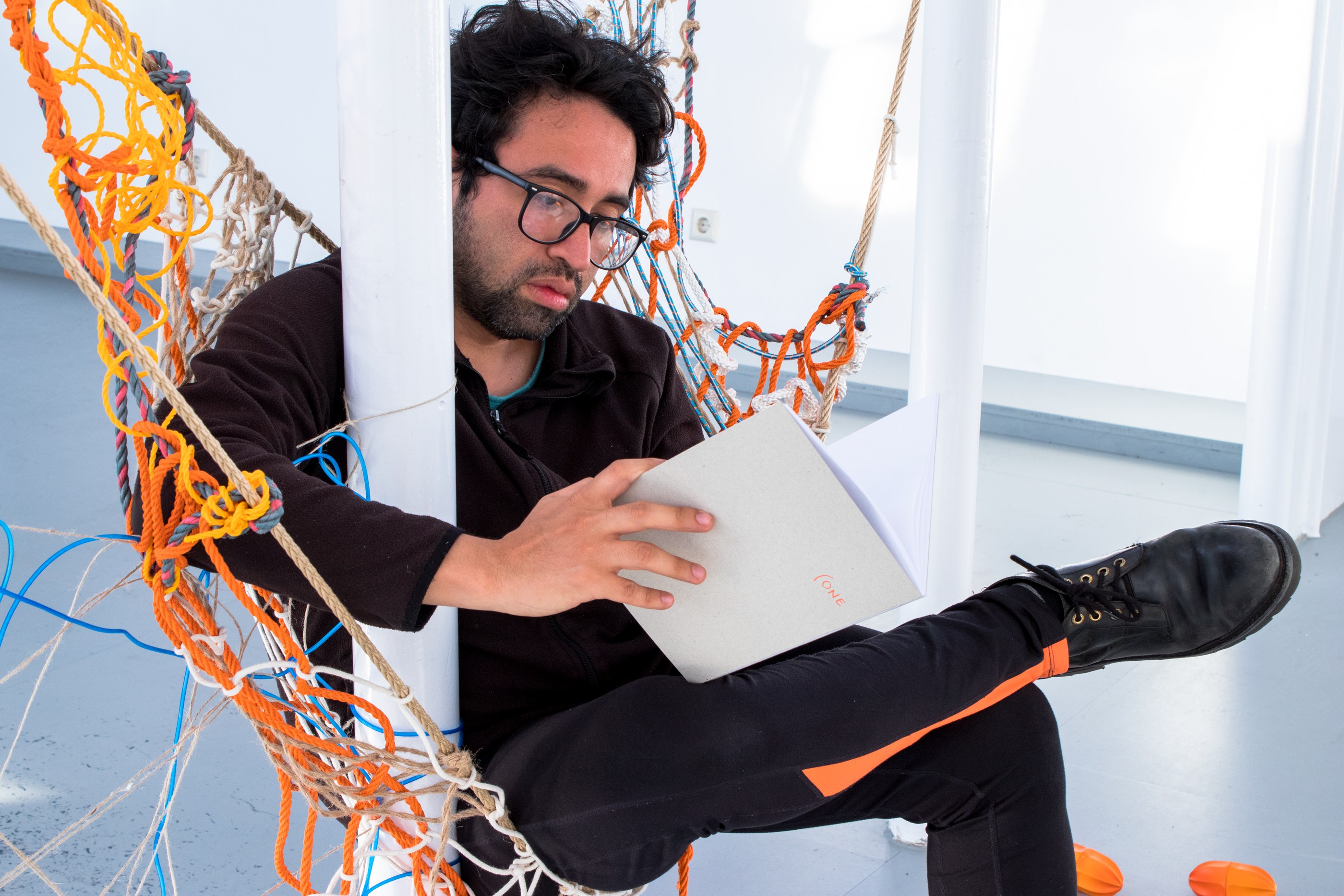 A person is reading a booklet sitting in a net hammock