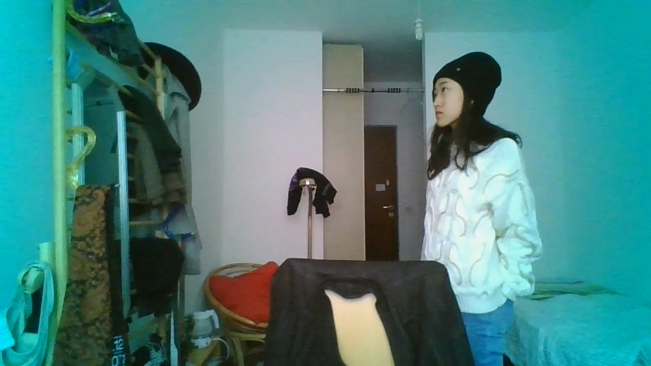 A person seen through a webcam, looking at their reflection in a mirror on the wall