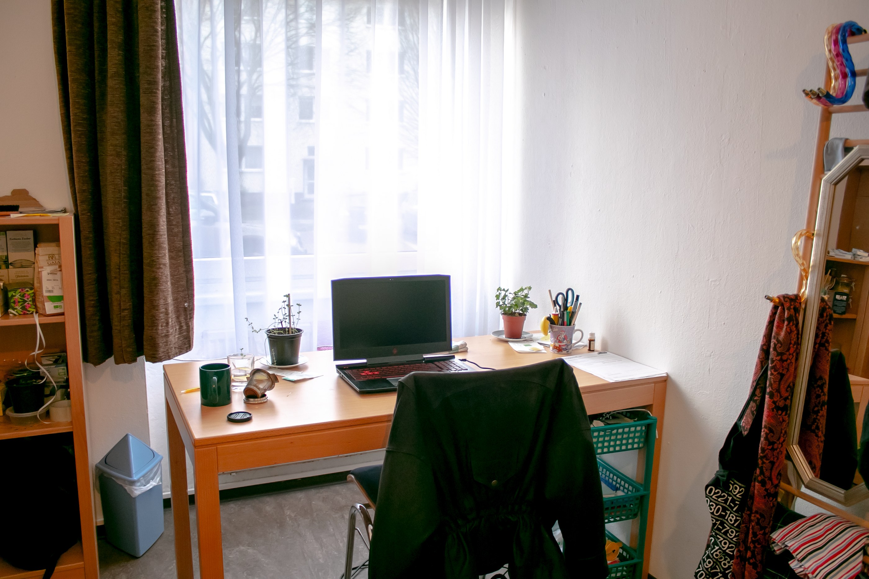 A laptop standing on a desk in a room, surrounded by everyday objects